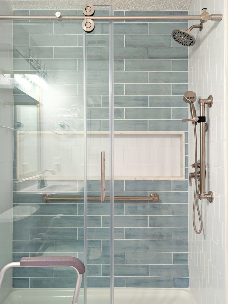 Image of shower after remodel. Image shows blue/green subway tile with grab bars and shower fixtures in satin nickel