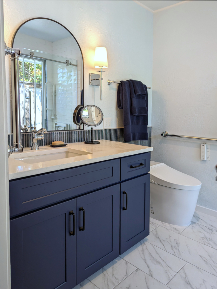 Small bathroom with blue vanity, chrome fixtures and black accent mirror and pulls. Elegant, transitional design. Marble look tile