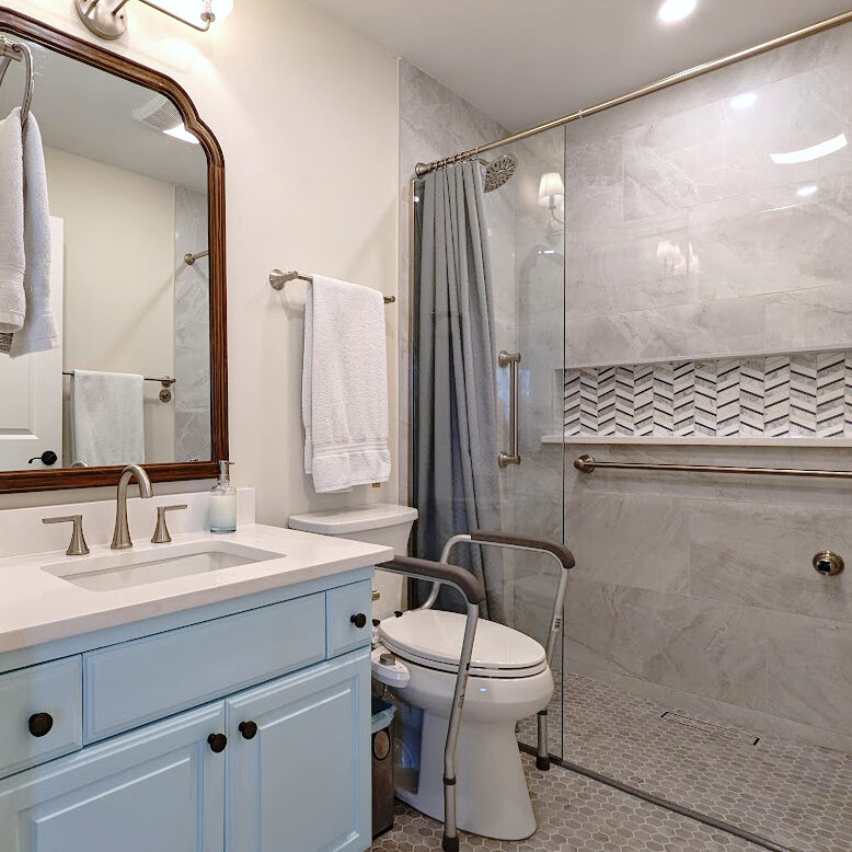Transitional accessible bathroom remodel with step free shower, comfort height toilet and grab bars. Gray, blue and wood tones